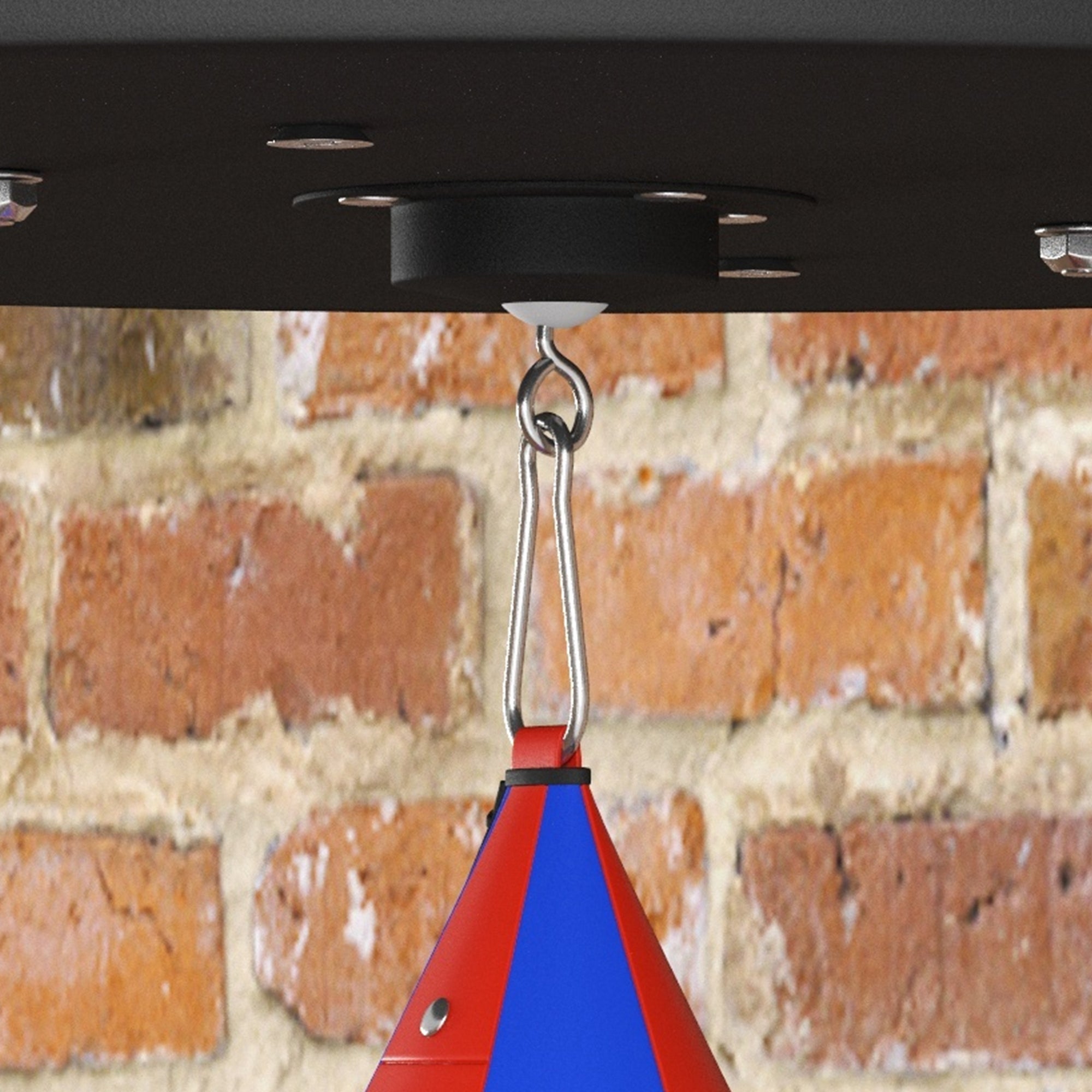 Red and blue punching bag hanging from a ceiling hook against a brick wall.