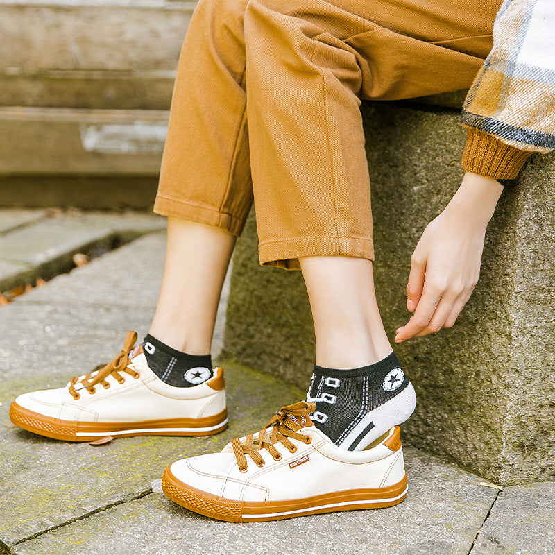 Person wearing white sneakers with brown soles and laces, sitting on a stone bench.