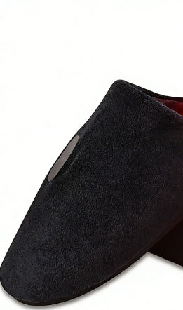 A close-up of a black suede slip-on shoe with a pointed toe and a small oval cutout on the side, set against a plain white background.