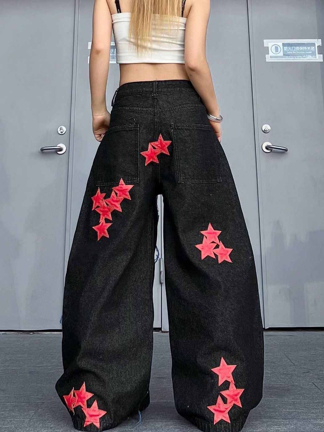 Person wearing black wide-leg pants with red stars in front of a gray door.