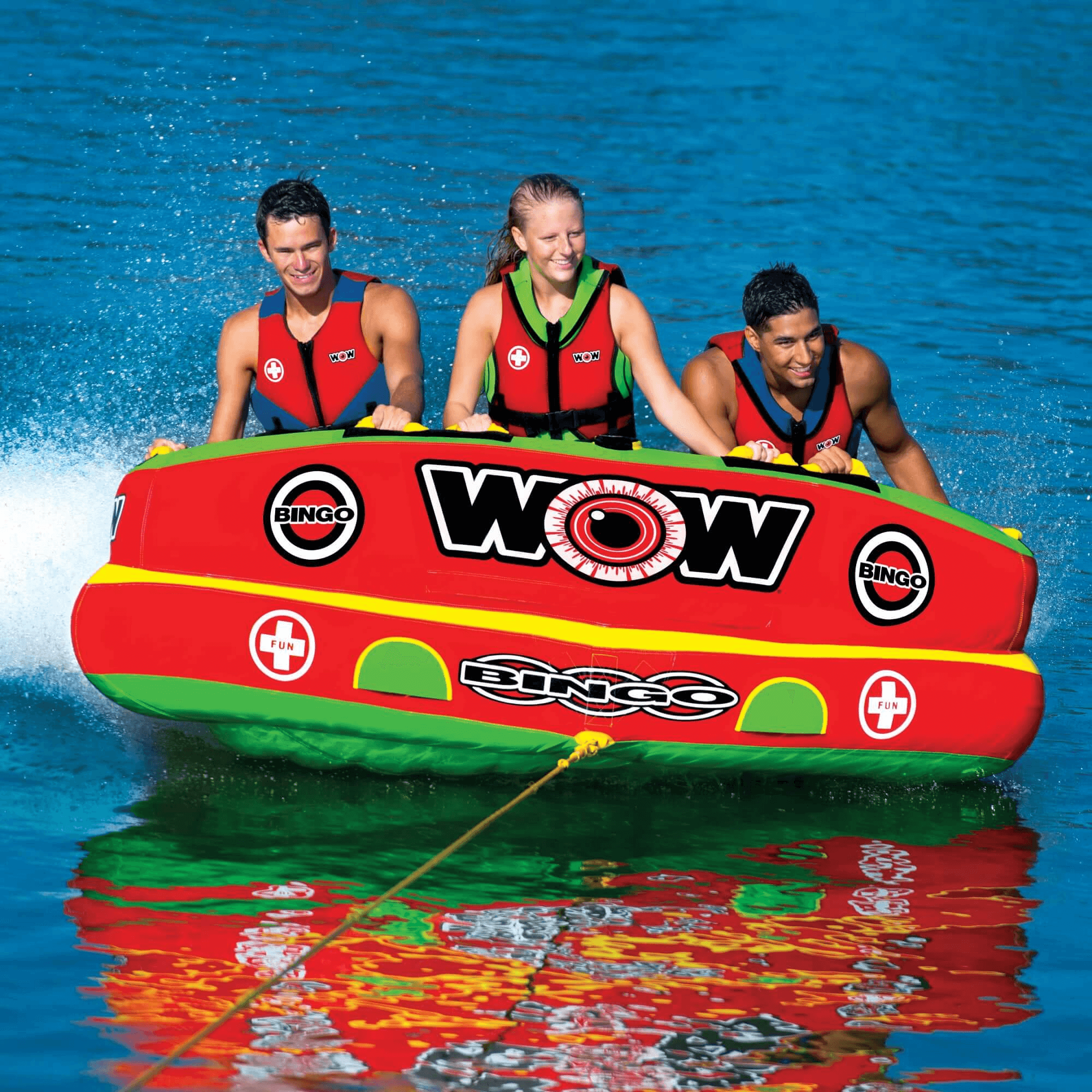 Three people on a red and green inflatable tube with 'WOW' branding in the water.