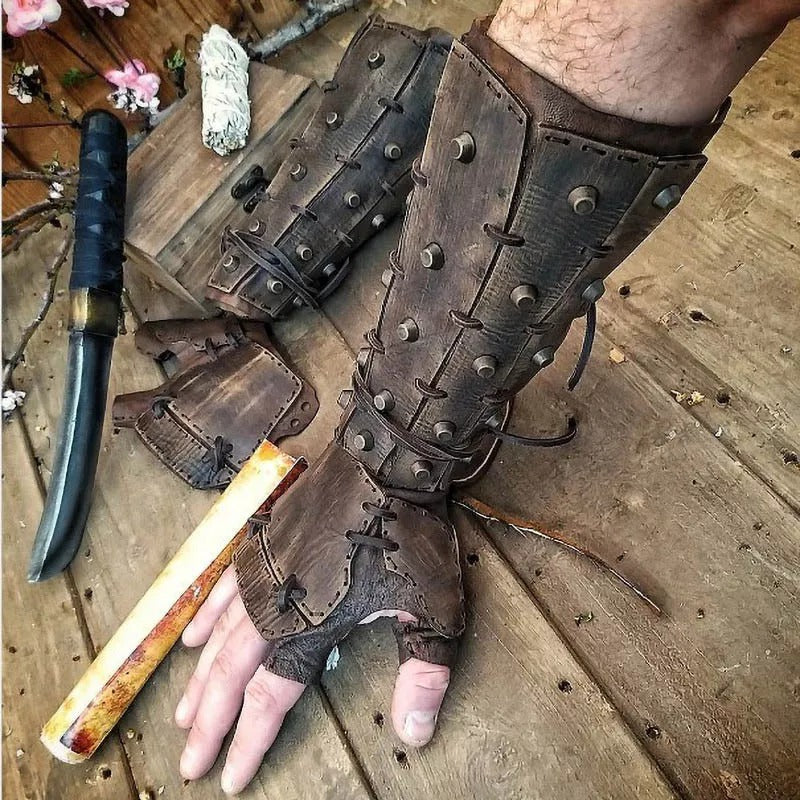 Brown leather gauntlets with metal studs on a wooden surface, accompanied by a knife and wooden stick.