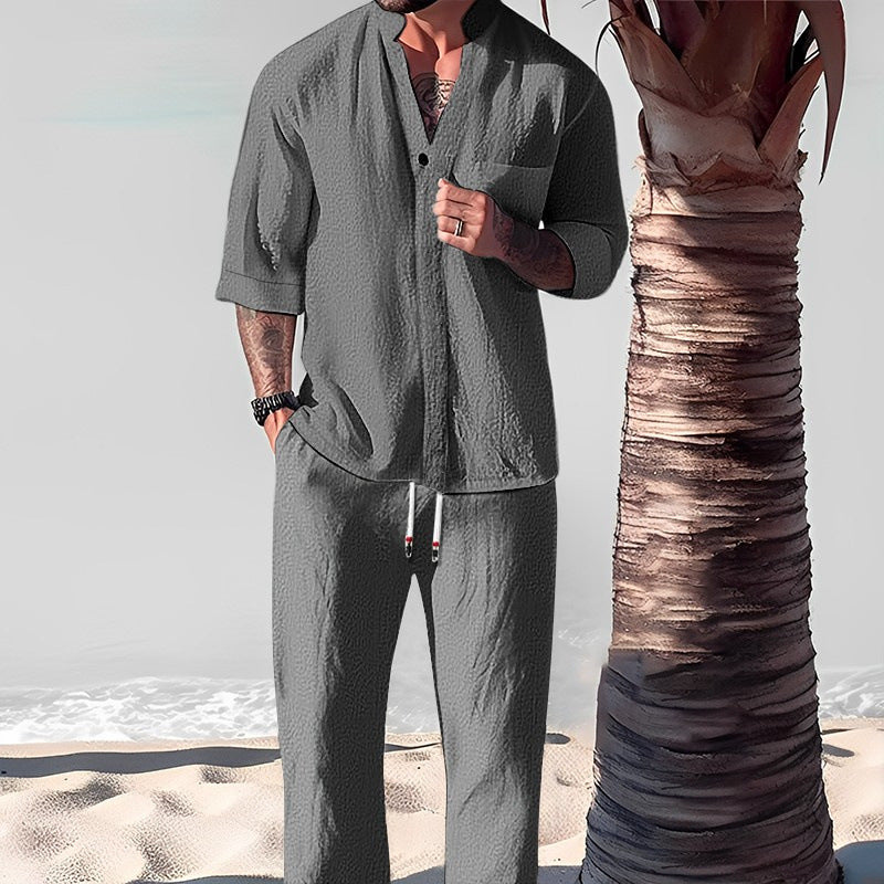 Person wearing a gray outfit standing on a beach with a palm tree.