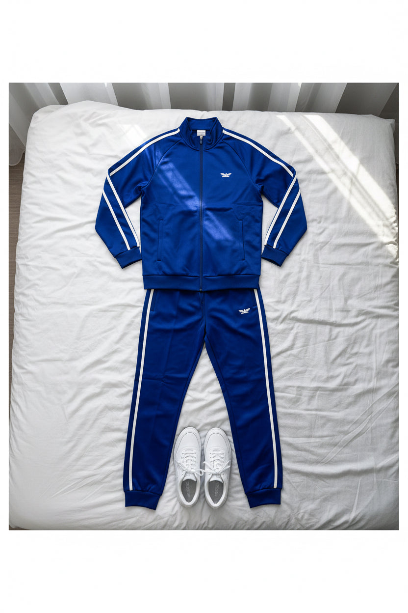 Person wearing a blue tracksuit with white stripes on a bed in background.
