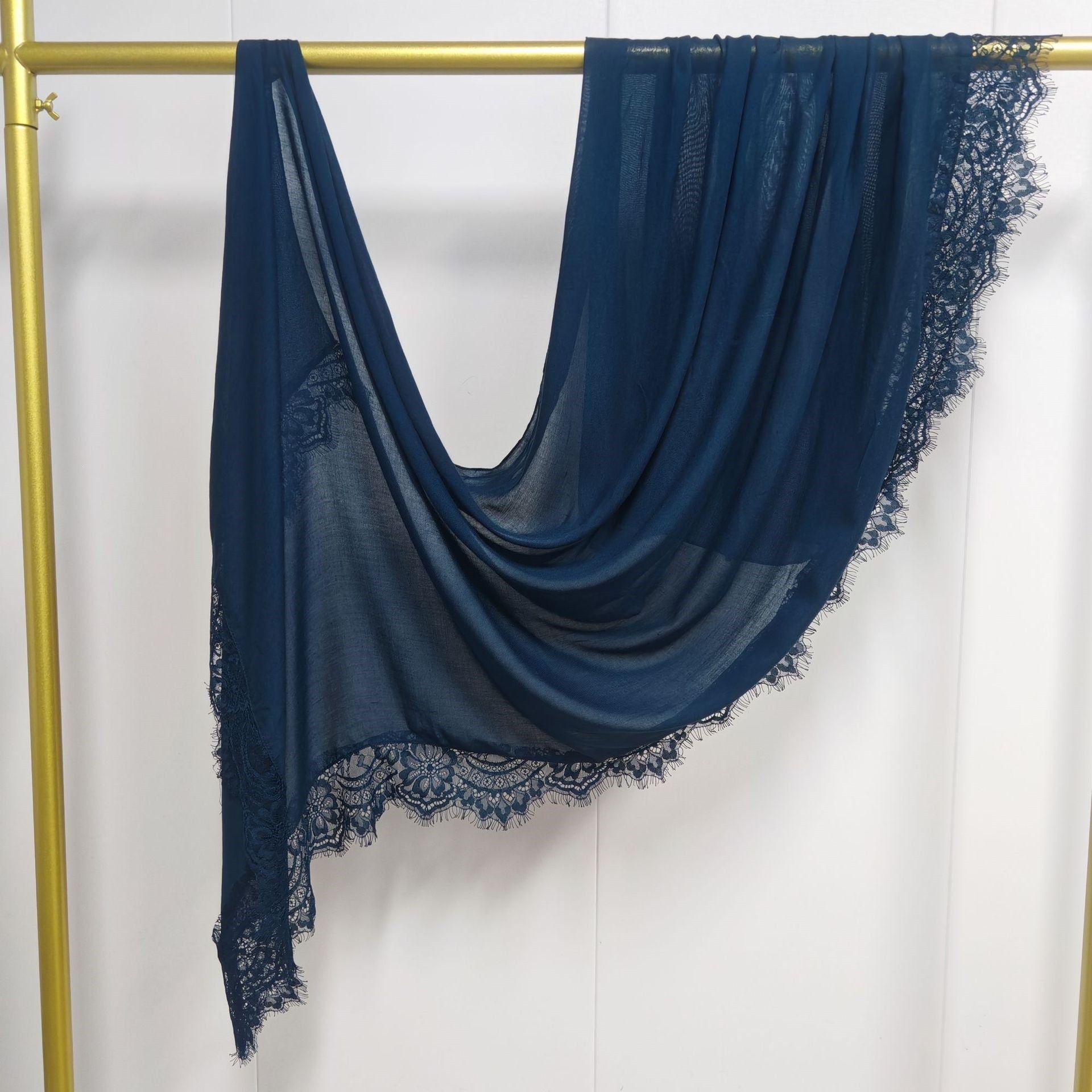 Navy blue scarf with lace trim draped over a gold rack on a white background