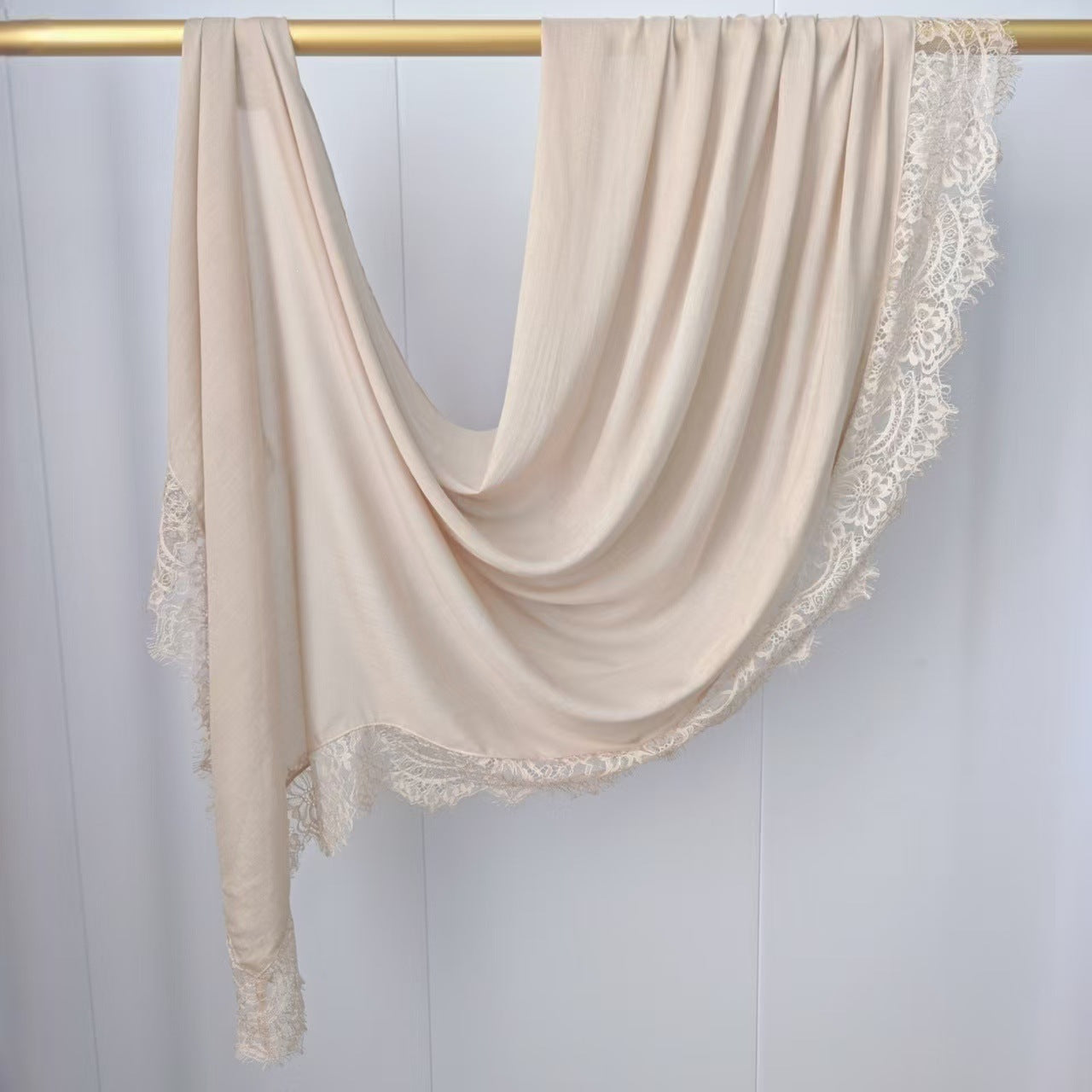 Beige scarf with lace trim draped over a gold rod on a white background