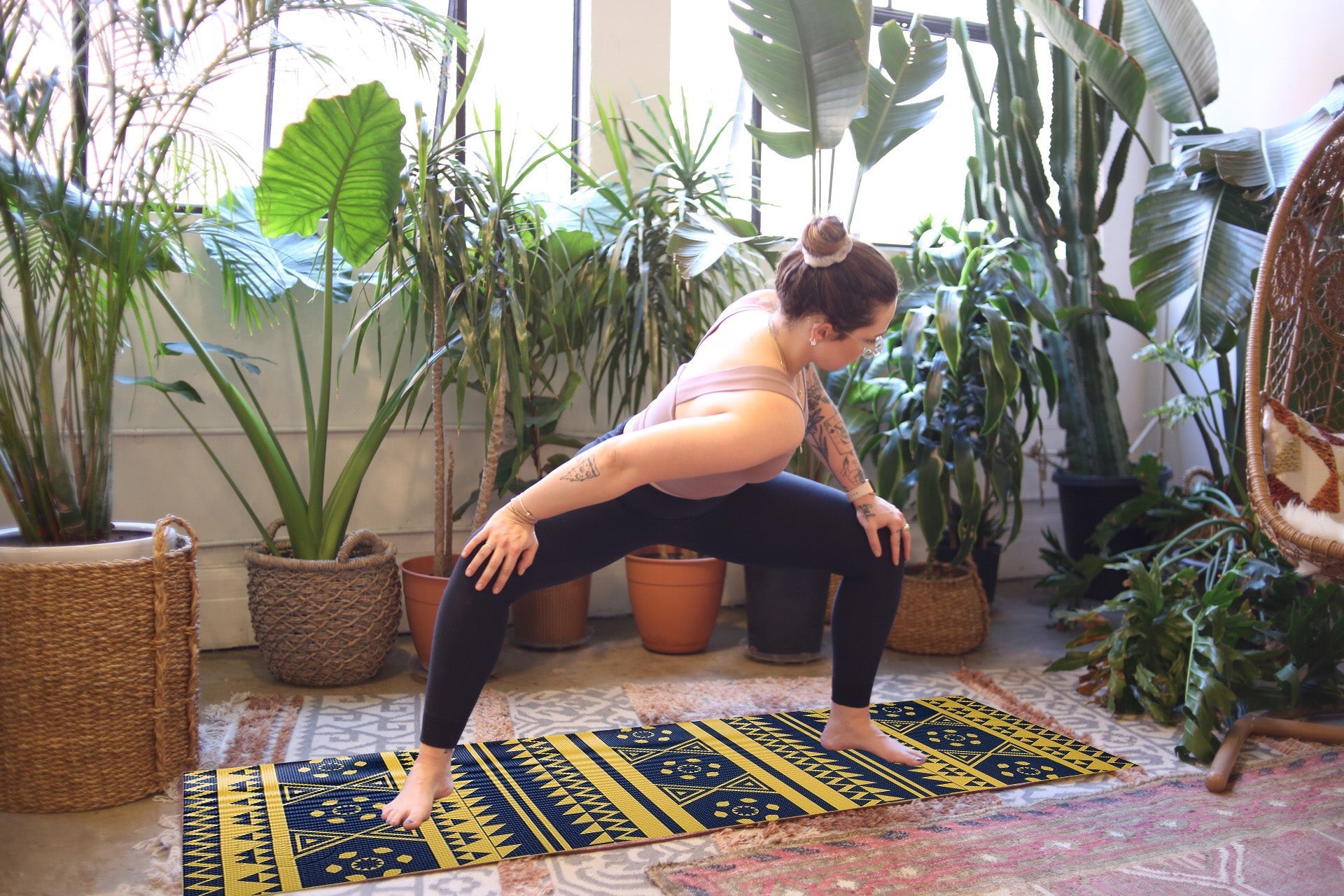Person practicing yoga on a colorful mat in a room with potted plants