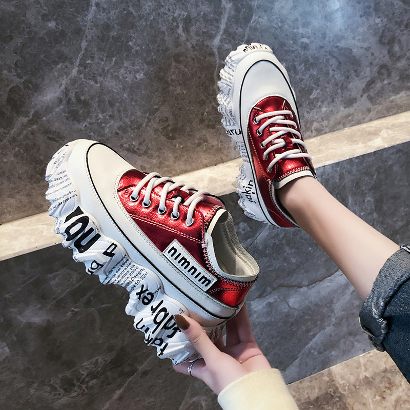 Red sneakers with white soles held by a person against a dark stone background