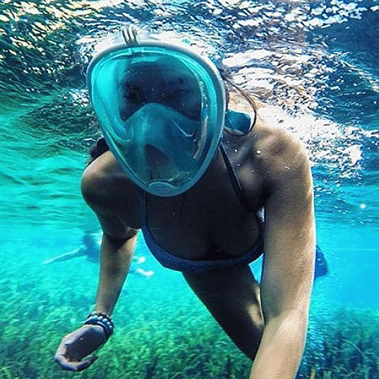 Person snorkeling in clear blue water wearing a full-face snorkel mask.