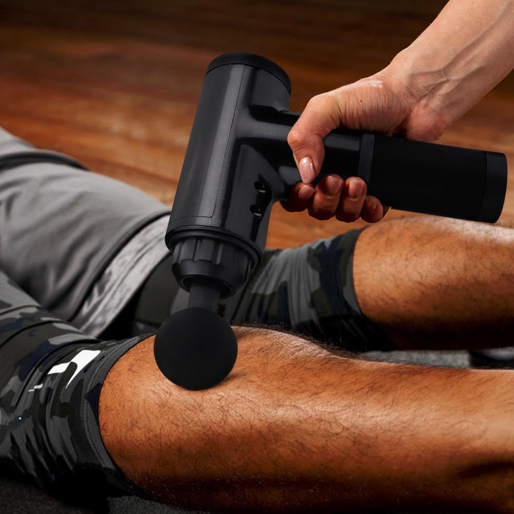 Person using a black massage gun on their leg with a wooden floor background